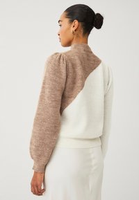 Maglione lavorato a maglia con colletto alto, maniche a palloncino e un design a colori blocco in tonalità di crema chiaro e taupe con una finitura testurizzata.