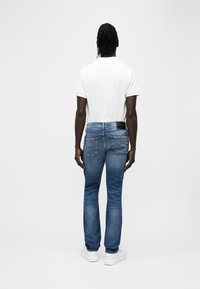 Μπλε τζιν παντελόνι με ίσια γραμμή, που διαθέτει δύο πίσω τσέπες και μαύρη ετικέτα στη μέση. Συνδυασμένο με λευκό μπλουζάκι και λευκά αθλητικά παπούτσια.