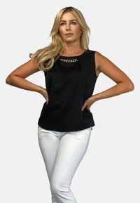 Czarny top bez rękawów z ozdobnym złotym łańcuchem na dekolcie, w zestawieniu z dopasowanymi białymi spodniami. Gładki materiał o luźnym kroju.