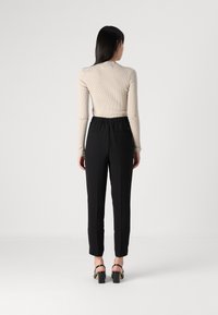 Top de manga larga de canalé beige combinado con pantalones negros de talle alto y corte tapered. Los pantalones tienen una cintura elástica y dos bolsillos traseros.