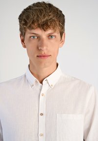 Camisa blanca de botón, en un tejido ligero y texturizado. Presenta un bolsillo en el pecho y botones en contraste, con un diseño de cuello relajado.