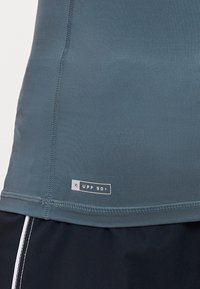 Blå prestasjonsdrakt laget av stretchy stoff med UPF 50+-merke, med rund hals og flate sømmer for komfort og holdbarhet.