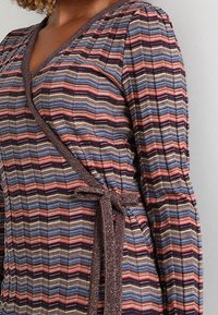 Robe portefeuille en tissu rayé multicolore avec un décolleté en V. Présente un matériau texturé et un accent noué à la taille.