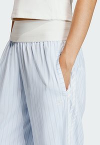 Jasnoniebieskie dresy w paski z elastycznym białym pasem, wyposażone w kieszenie i subtelne haftowane logo. Gładka faktura materiału.