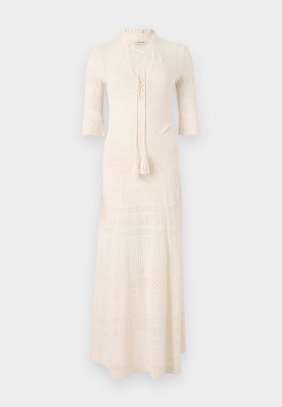 Gebreide maxi-jurk in crème met een hoge hals, halve mouwen en een textuurpatroon. Kenmerkt zich door een striksluiting en kwastjes detail bij de taille.