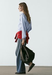 Hellblau gestreiftes Hemd mit Knöpfen, roter Pullover um die Taille gebunden, weit geschnittene Jeans und eine braune Lederhandtasche. Glatte Texturen, neutrale Farben.