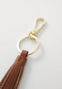 Porte-clés en cuir marron avec un fermoir en métal doré et un anneau circulaire, comportant un logo en relief sur l'anneau.