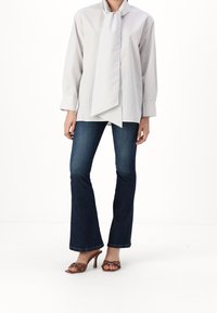 Vit långärmad skjorta med grå ränder, med en slipskrage, i kombination med mörkblå utsvängda jeans och bruna klacksandaler.