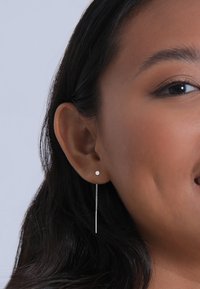 Pendientes de plata con un pequeño stud redondo y una cadena larga y delgada que cuelga. Textura suave con un acabado pulido. Diseño simple y moderno.