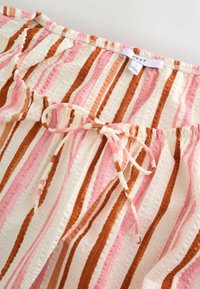 Pruhovaná látka s růžovými, hnědými a krémovými svislými pruhy, s vázacím šňůrkou a štítkem značky "NEXT".