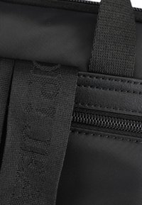 Sección de bolsa de tela negra con correas texturizadas y un zipper. El material parece duradero, con un acabado liso y mate.