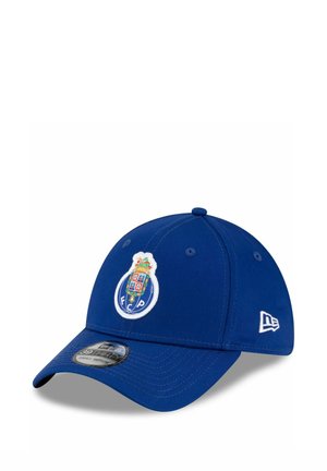 Gorra de béisbol azul con un logo de escudo que presenta un escudo y una corona en la parte delantera, y un logo de marca bordado en blanco en el lateral.