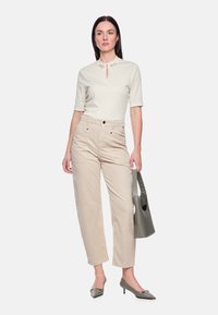 Beige Baumwollbluse mit dekorativem Ausschnitt, kombiniert mit hellbraunen Cordhosen. Graue Handtasche und passende graue spitze High Heels.