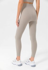 Világos bézs bordázott leggings magas derékkal, testhezálló fazonnal és sima textúrával, fehér és szürke sportcipővel párosítva.