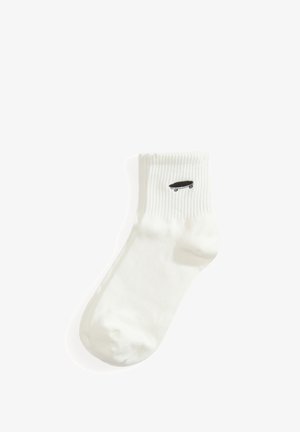 Hvid ankelstrømpe med ribbet kant og lille sort skateboardikon broderet nær toppen.