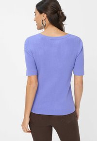 Paarse geribbelde top met korte mouwen en een wijde halslijn. Strak ontwerp en gladde textuur. Gekleed met bruine broek, getoond vanuit de achterkant.