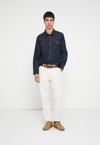 Sötétkék farmering két első zsebbel, fehér pamutnadrág és világosbarna, fűzős cipő. Egyszerű, tiszta kialakítás, klasszikus szabás.