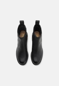 Botines negros de cuero con paneles elásticos en los laterales y tiradores; textura suave, puntera redondeada y un diseño minimalista.