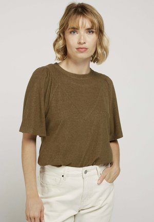 Haut brun à manches courtes avec un col rond et un tissu texturé. Présente un design de couture diagonale. Associé à un jean blanc taille haute.