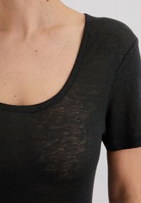 Maglietta nera a maniche corte con scollatura rotonda, caratterizzata da una texture leggermente trasparente e un tessuto morbido e leggero. Nessun motivo o dettaglio visibile.