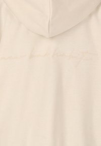 Cremfarbene Kapuzenjacke mit weicher Textur, die auf dem Rücken eine dezente gestickte Phrase "neue schlechte Gewohnheiten" zeigt.