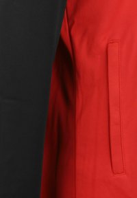 Veste rouge et noire avec des sections contrastées, tissu lisse, dotée d'une poche latérale sur le panneau rouge, design ajusté.