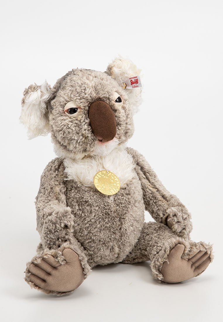 Plüschkoala mit grauem Plüschfell, weißen Akzenten, einer braunen Nase und beigen Pfoten. Verfügt über eine goldene Medaille und ein Etikett am Ohr.