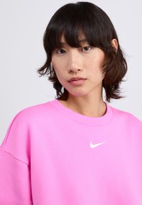Sweatshirt Nike rose avec un col rond, arborant un logo blanc sur la poitrine. Le tissu est léger et doux, offrant une coupe décontractée.