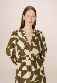 Robe à manches longues en vert olive avec de grands motifs abstraits blancs, dotée d'un col à boutons et d'une taille élastiquée pour un ajustement parfait.