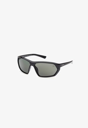 Schwarze Kunststoffsonnenbrille mit grauen Gläsern, kantigem Design, dicken Rahmen und glänzender Oberfläche. Logo auf der Seite des Rahmens sichtbar.