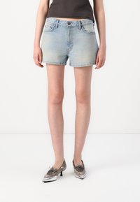 Shorts en denim délavé avec une coupe droite, un ourlet retroussé, des poches avant et une fermeture à bouton. Associés à des chaussures à talons bas métalliques.