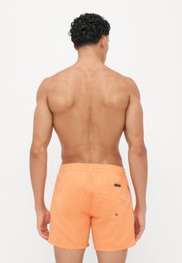 Pantaloni scurți de înot portocalii, realizați dintr-un material ușor, având talie elastică și un buzunar posterior cu detaliu cu apăsare.