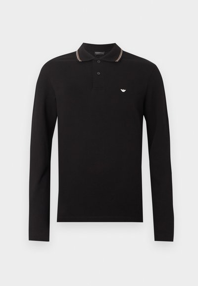 Μαύρο μακρυμάνικο πόλο πουκάμισο με πατιλέτα δύο κουμπιών, ριμπ κολάρο με λευκές και πορτοκαλί ρίγες, και μικρό λευκό λογότυπο αετού στο στήθος.