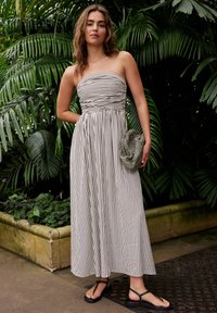 Trägerloses Maxikleid mit vertikalen schwarz-weißen Streifen, geraffter Taille, kombiniert mit einer strukturierten Clutch und flachen schwarzen Sandalen.