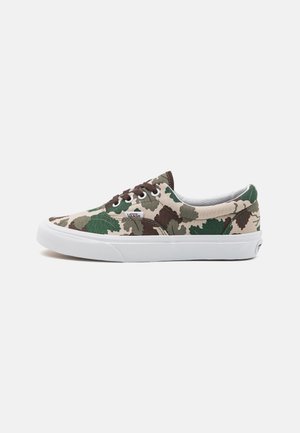 Niskie buty sportowe Vans z zielonym, brązowym i beżowym wzorem moro, białą gumową podeszwą i ciemnobrązowymi sznurowadłami na jednolitym tle.