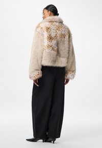 Kurtka z futerka sztucznego w beżowym i kremowym kolorze z cętkowanym wzorem. Posiada krótki krój i szerokie rękawy. Zestawiona z czarnymi spodniami o szerokich nogawkach.