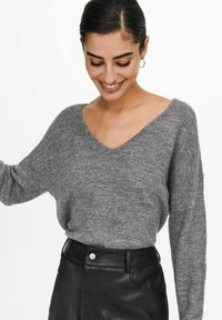 Grijze gebreide trui met een V-hals, losse pasvorm, gezakte schouders en lange mouwen, gecombineerd met een zwart leren rok met hoge taille.