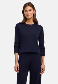 Granatowy dzianinowy sweter z okrągłym dekoltem, długimi rękawami i luźnym krojem, w zestawie z dopasowanymi spodniami. Gładka tekstura, minimalistyczny design.