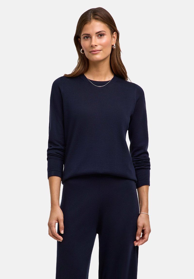 Granatowy dzianinowy sweter z okrągłym dekoltem, długimi rękawami i luźnym krojem, w zestawie z dopasowanymi spodniami. Gładka tekstura, minimalistyczny design.