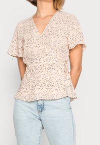 Blusa beige con estampado floral, con escote en V, mangas cortas con vuelo y dobladillo ligeramente acampanado, confeccionada en tela ligera.