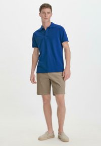 Blue polo shirt in a classic fit, paired with light brown shorts. The shirt features a collar and short sleeves, and the shorts have a straight cut.