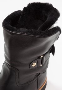Black leather boot with a plush black fur lining at the top, featuring a gold-toned metal buckle and robust sole.