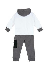 Ensemble sweat à capuche et pantalon en coton blanc et gris. Le haut possède des poignets gris ; le pantalon est doté d'une poche cargo noire sur la jambe gauche.