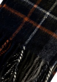 Detailní záběr na tmavou vlněnou šálu s oranžovým a bílým kostkovaným vzorem a třásněmi na koncích.