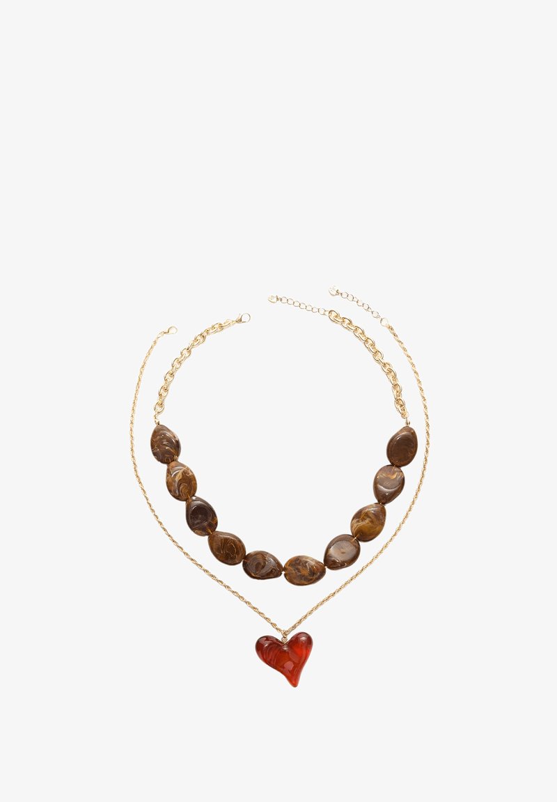 Náhrdelník se dvěma řetězy; jeden zlatý kov a jeden s hnědými mramorovými korálky. Uprostřed červený přívěsek ve tvaru srdce. Texturované a hladké plochy.