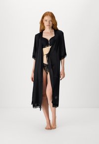 Svart satengpajama med belte i midjen, korte ermer og blondebesetning langs kantene, lagd over blondeundertøy.