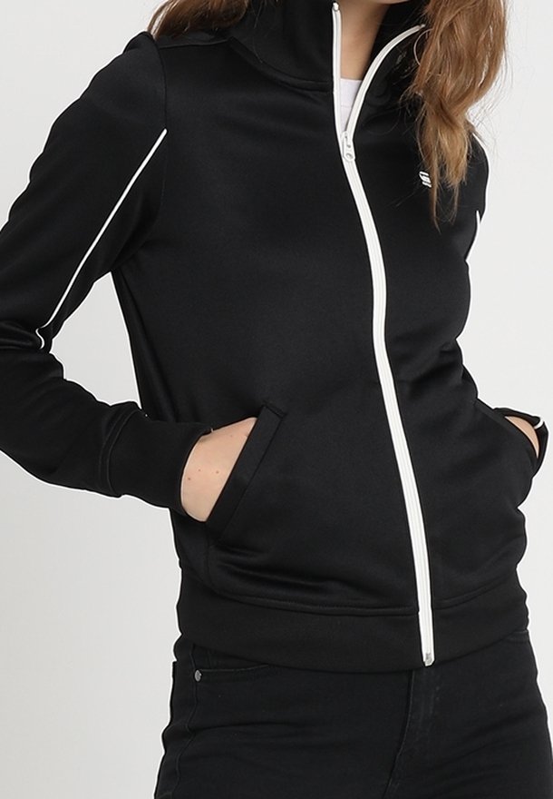 Chaqueta negra con cremallera, hecha de un tejido suave, con detalles de ribete blanco en los hombros, cuello alto y bolsillos laterales.