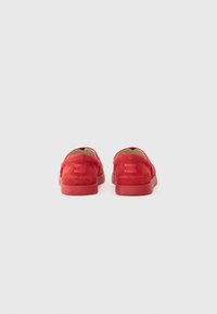 Pantofi slip-on roșii, realizați din piele ante, cu o textură netedă, formă rotundă, design minimalist și branding embosat pe toc.
