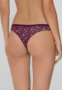 String en dentelle floral bourgogne avec une taille basse, présentant un motif délicat de fleurs roses sur un fond de tissu transparent.