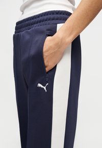 Παντελόνια αθλητικά σε ναυτικό μπλε με υφασμένο ζωνάρι μέσης, αντίθετες λευκές ρίγες στο πλάι και τσέπη με φερμουάρ που διαθέτει λευκό λογότυ πο.